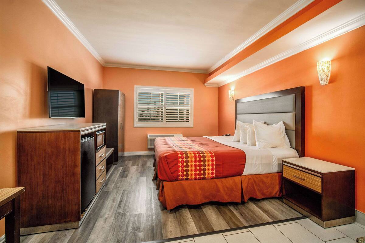 Een slaapkamer met een bed, nachtkastjes, een kledingkast, een raam met jaloezieën en een aan de muur bevestigde televisie.