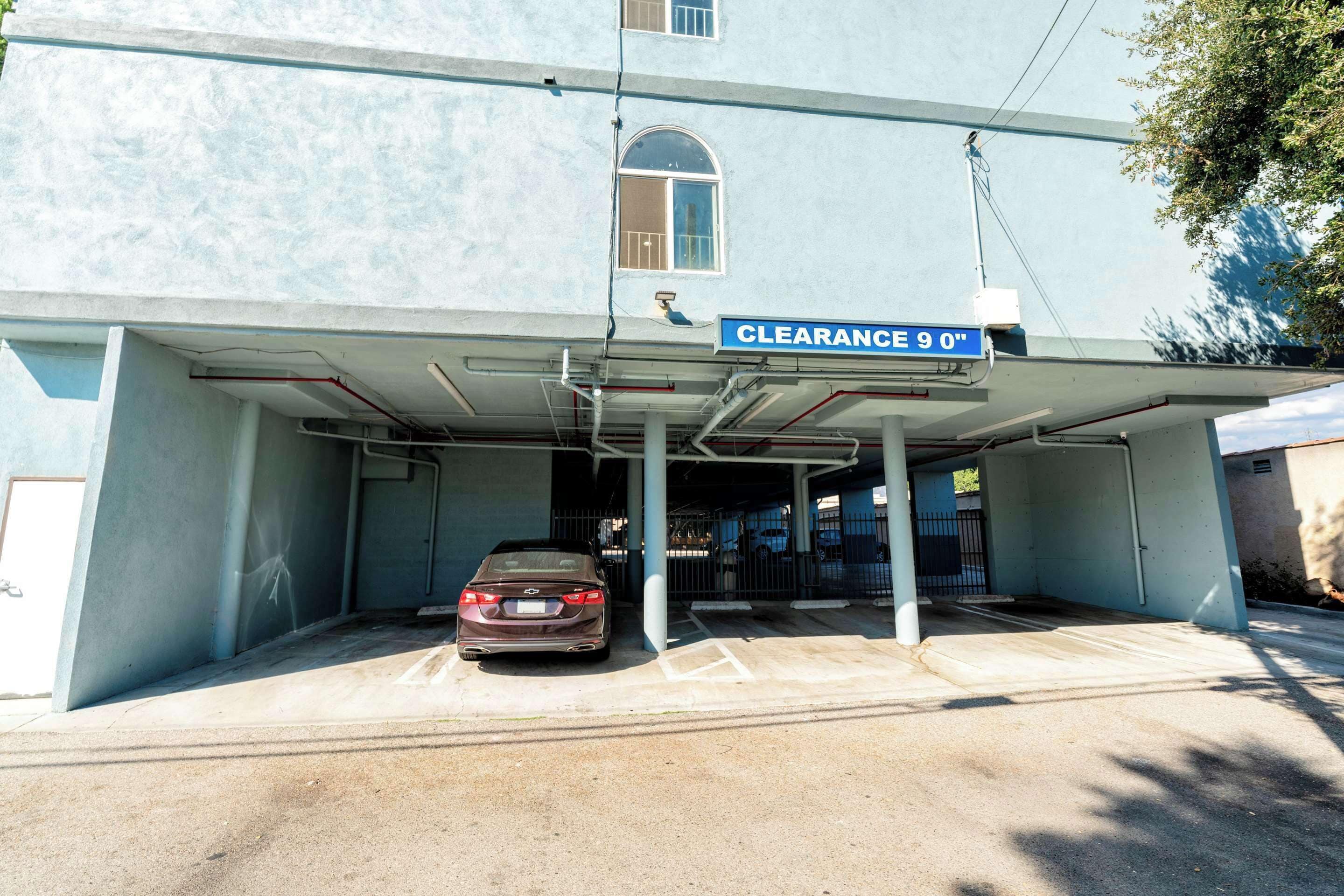 Entrada de estacionamiento con un letrero de altura máxima de 9 pies, un coche dentro y un edificio de fachada azul.