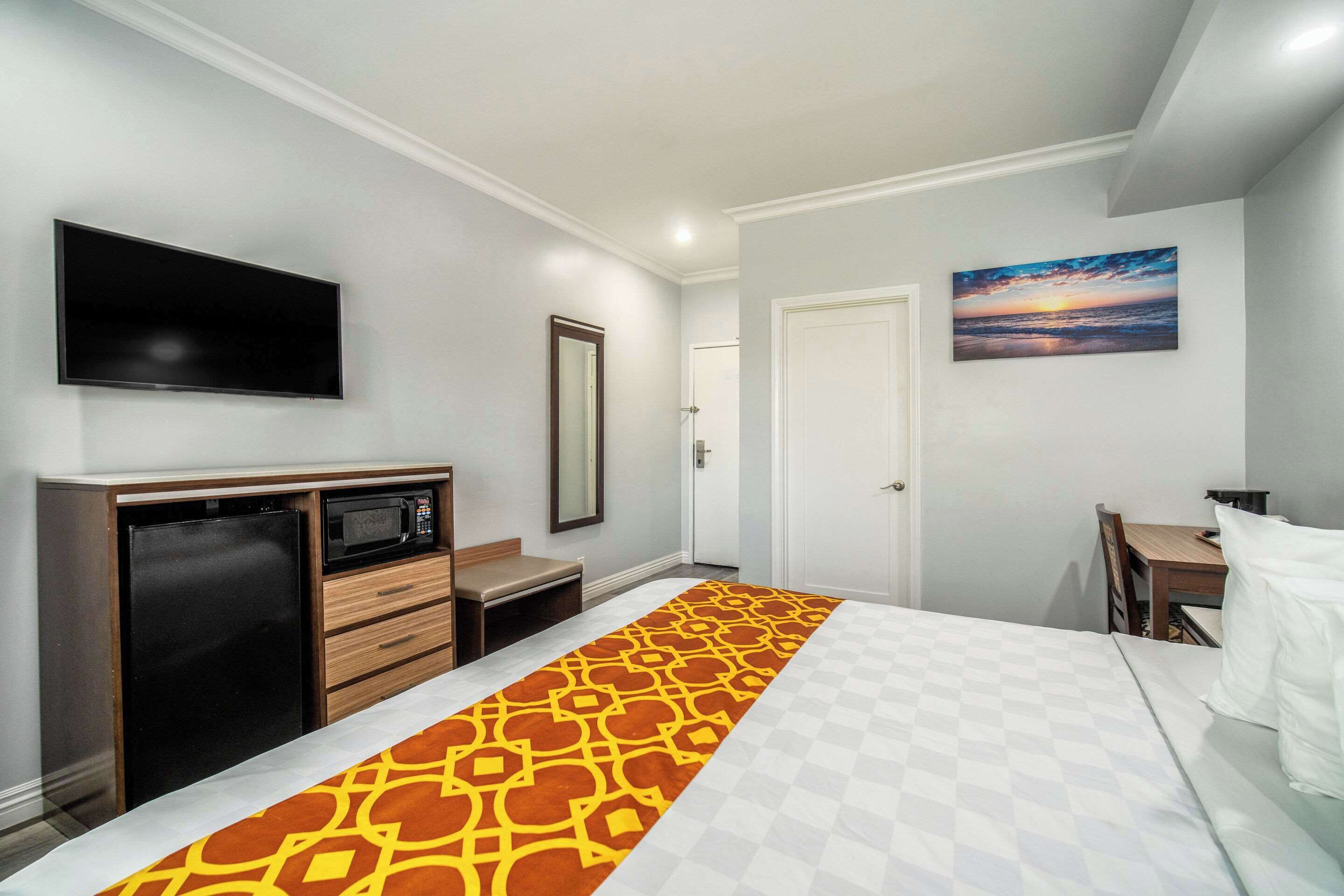A hotel room with a bed, a TV, a microwave, a refrigerator, a desk, and a door.