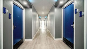 Un pasillo de hotel con puertas azules, placas de números de habitaciones y suelo de madera.