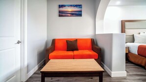Una habitación de hotel moderna con una mesa de centro de madera, un sofá naranja con un cojín marrón y un cuadro de un atardecer en la pared.