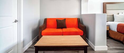 Una habitación de hotel moderna con una mesa de centro de madera, un sofá naranja con un cojín marrón y un cuadro de un atardecer en la pared.