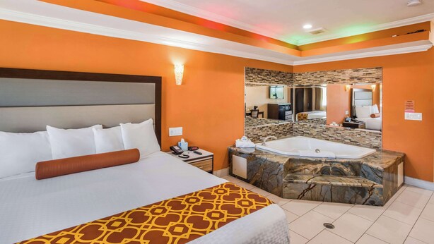 Una habitación de hotel con una cama grande, un baño con bañera de mármol y paredes naranja.