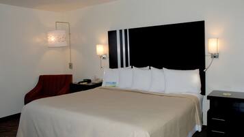 Quarto de hotel com uma cama grande, duas mesas de cabeceira, uma cadeira vermelha e duas luminárias fixadas na parede.
