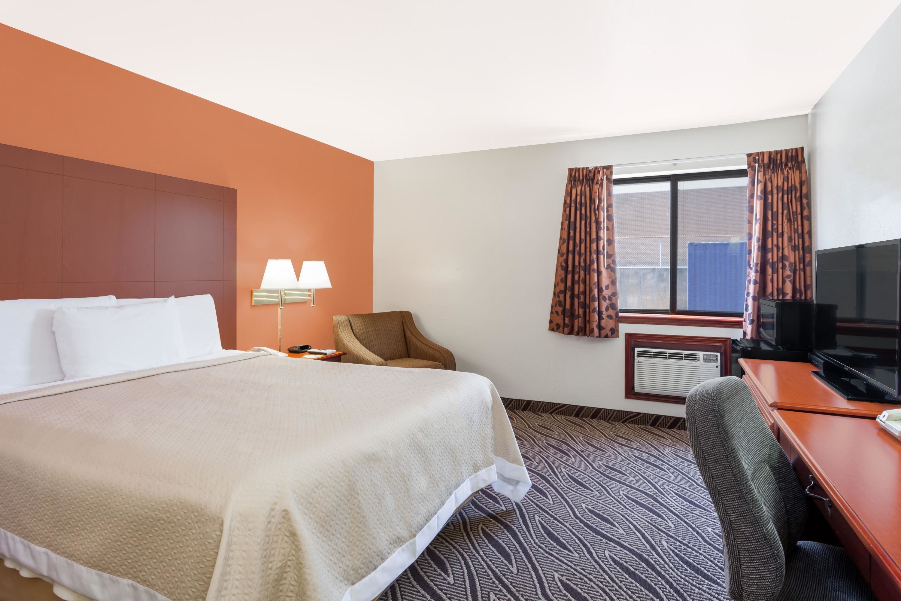 Une chambre d’hôtel équipée d’un lit, d’un bureau, d’une chaise, d’une télévision, d’une lampe et d’une fenêtre avec des rideaux.