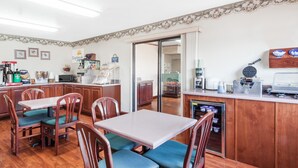 A dining area with wooden tables and chairs, a refrigerator, and a kitchen area with cabinets and appliances.