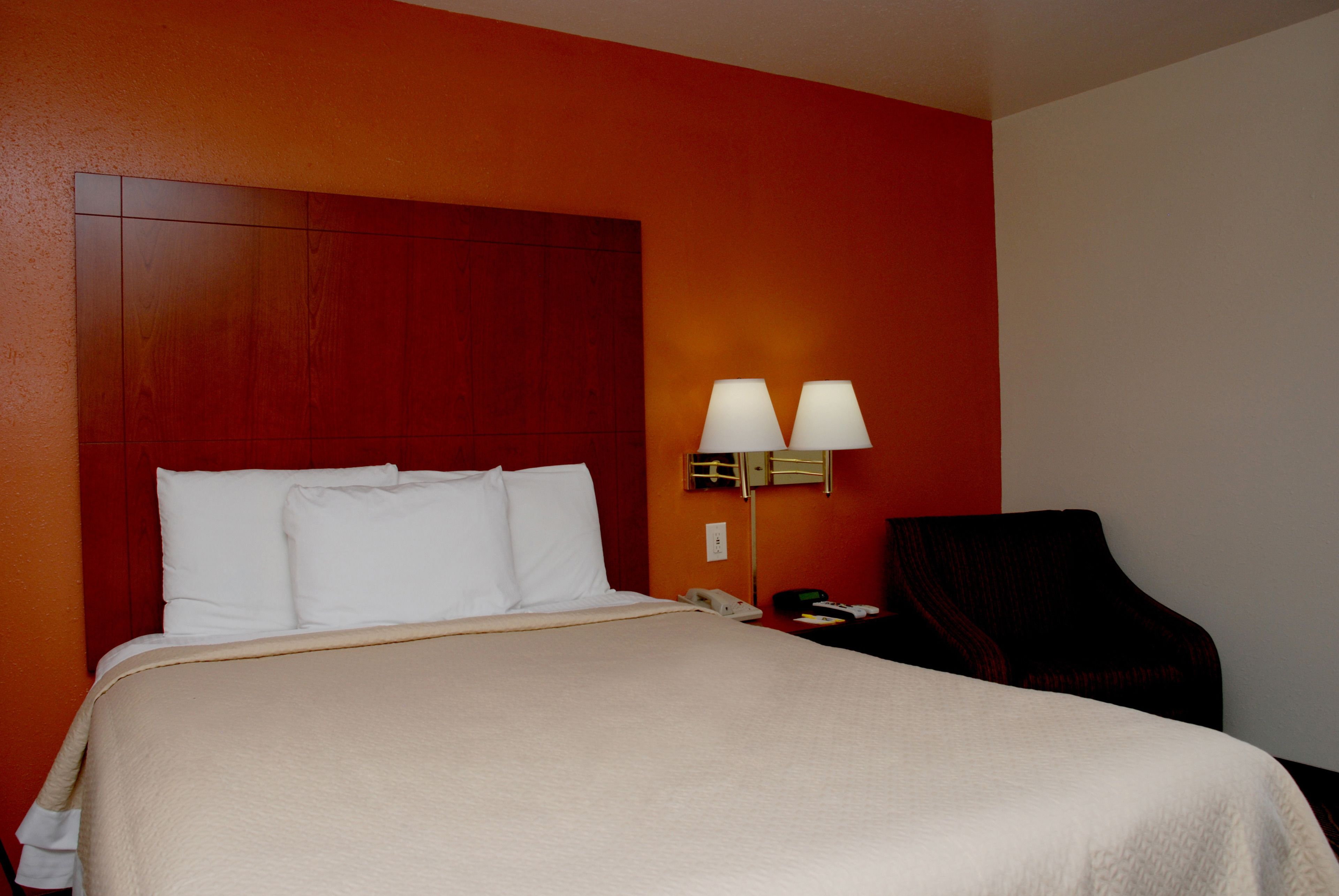A hotel room with a large bed, two bedside lamps, a telephone, and a chair.