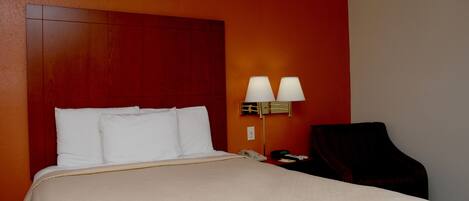 A hotel room with a large bed, two bedside lamps, a telephone, and a chair.
