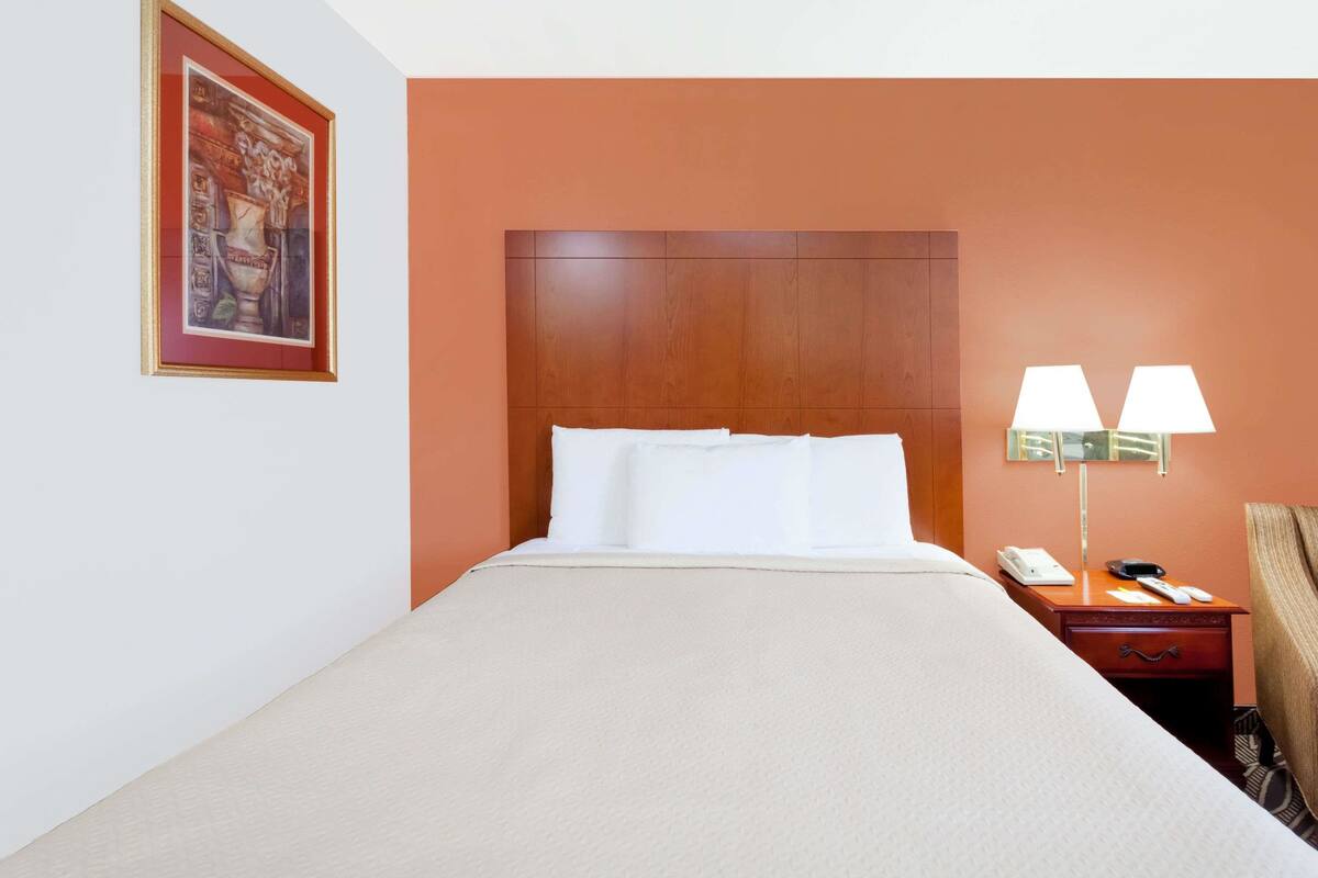 A hotel room with a large bed, a wooden headboard, a nightstand with a lamp, and a painting on the wall.