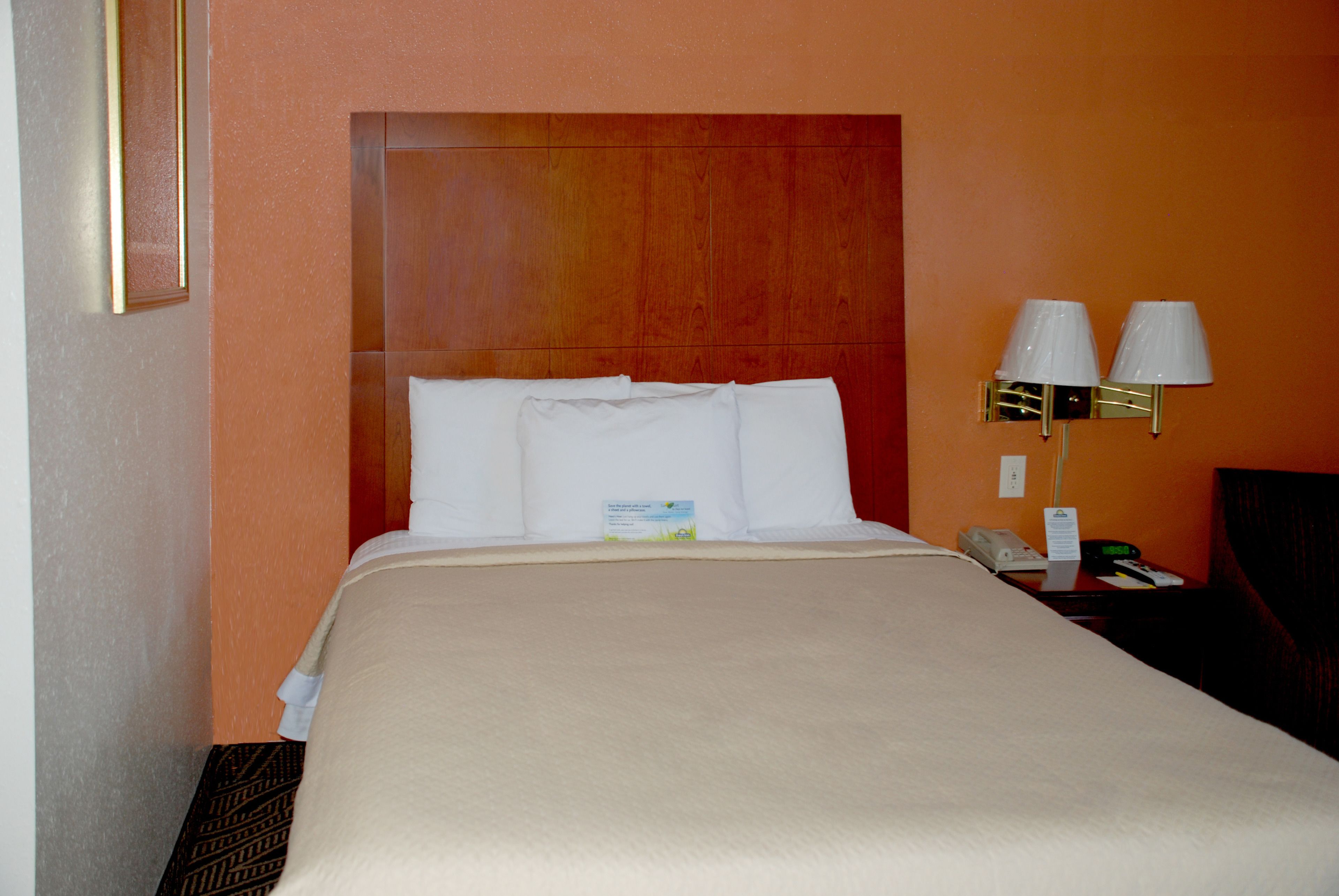 Habitación de hotel con una cama grande, cabecera de madera, dos lámparas de noche y una mesita de noche con teléfono y lámpara.
