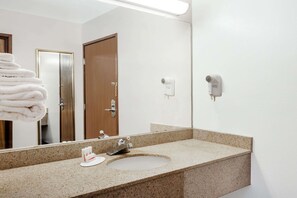 A hotel bathroom with a granite countertop, a sink, a mirror, a towel rack with folded towels, a hair dryer, and a door. - Days Inn by Wyndham Dyersburg (Dyersburg)