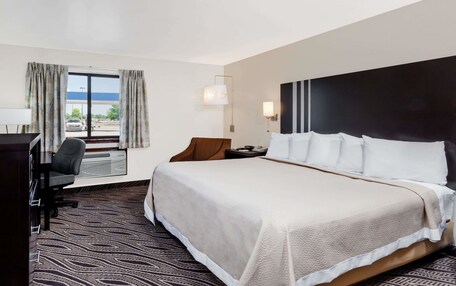 A hotel room with a large bed, a desk with a chair, a window with curtains, and a view of a parking lot.