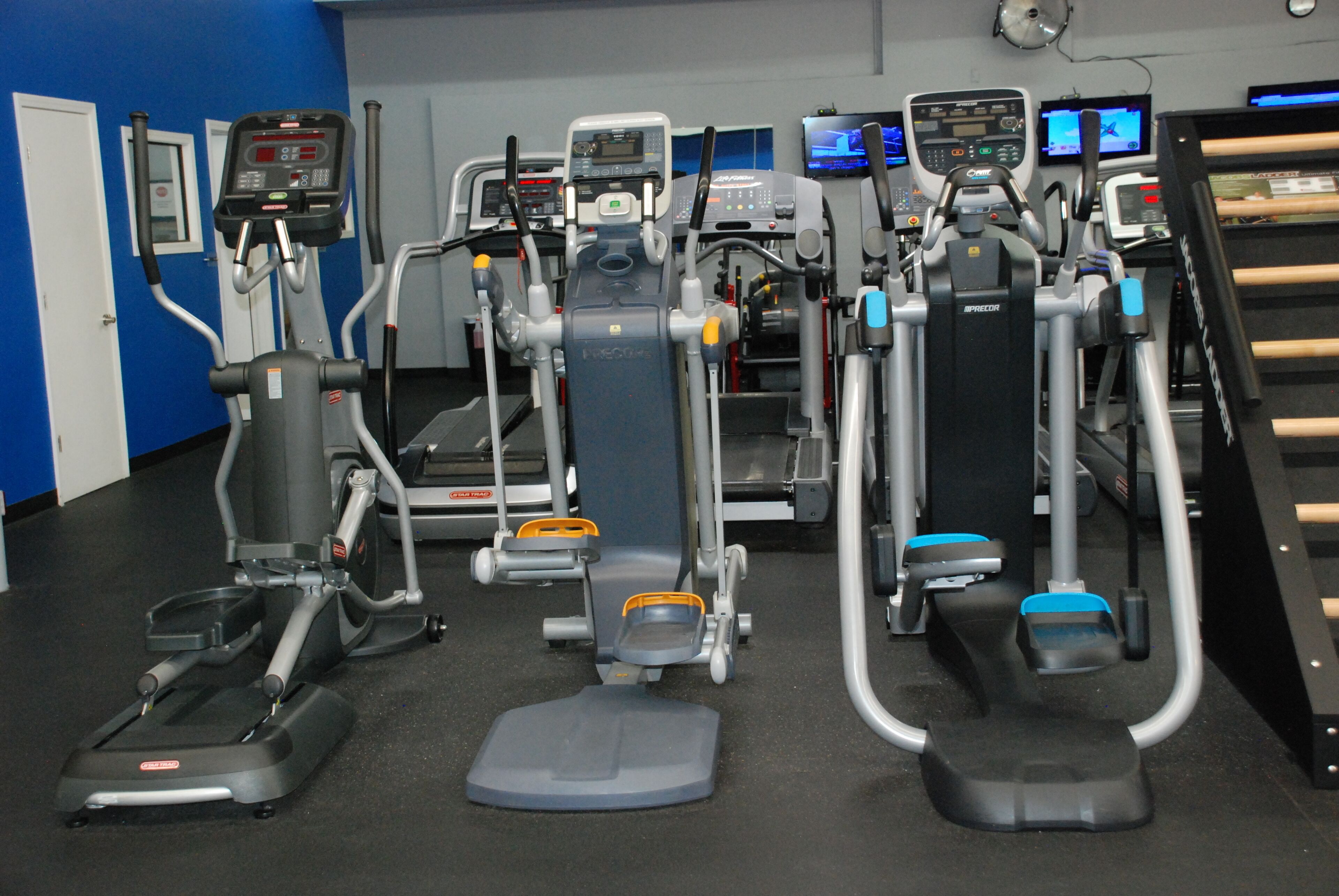 Un gimnasio con diversas máquinas de ejercicio, incluyendo cintas de correr y elípticas, dispuestas en filas.