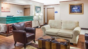 A hotel lobby with a reception desk, a brown leather armchair, a beige sofa, and a striped rug.