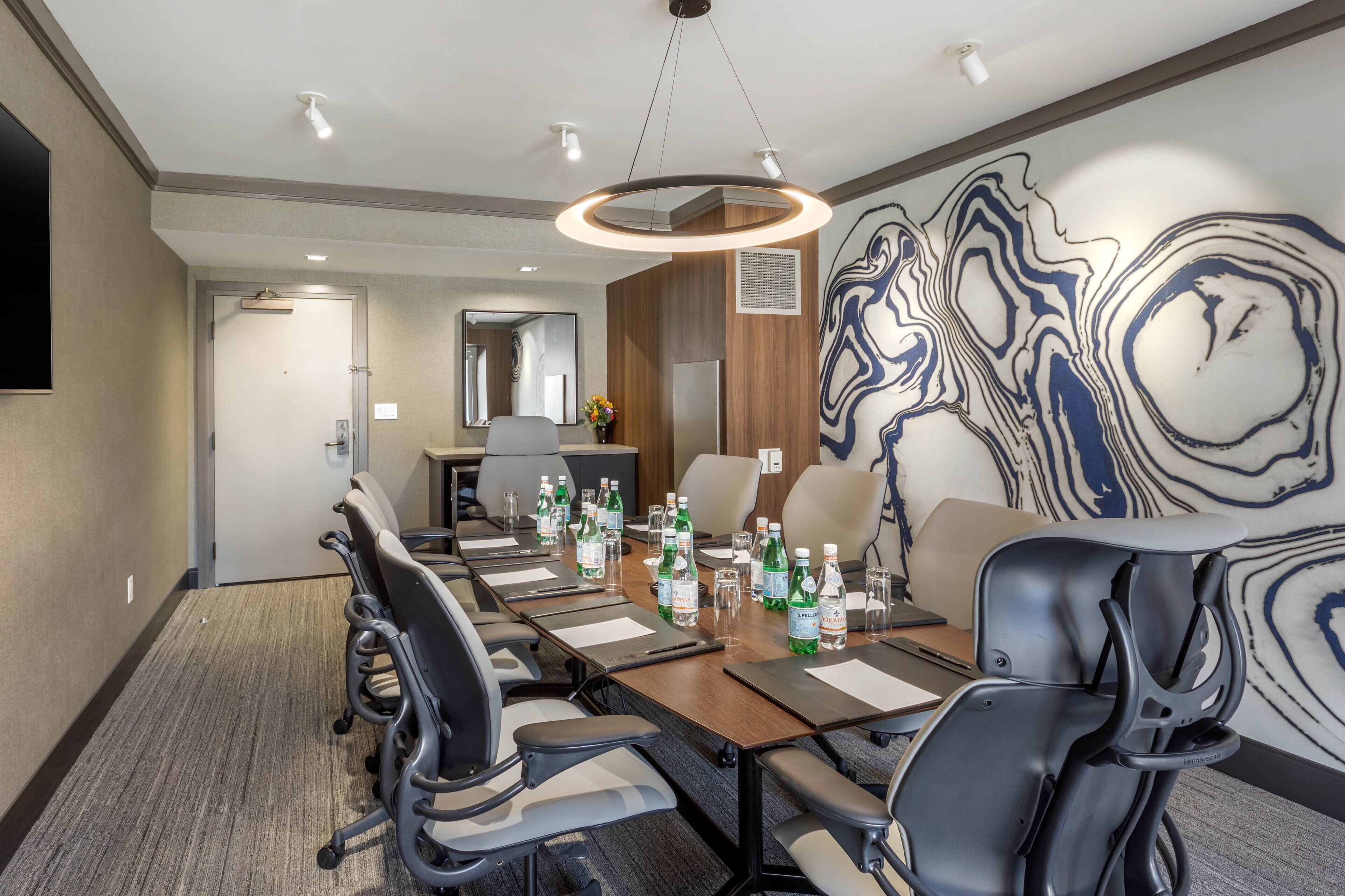 A conference room with a long table, chairs, and a large abstract mural on the wall.