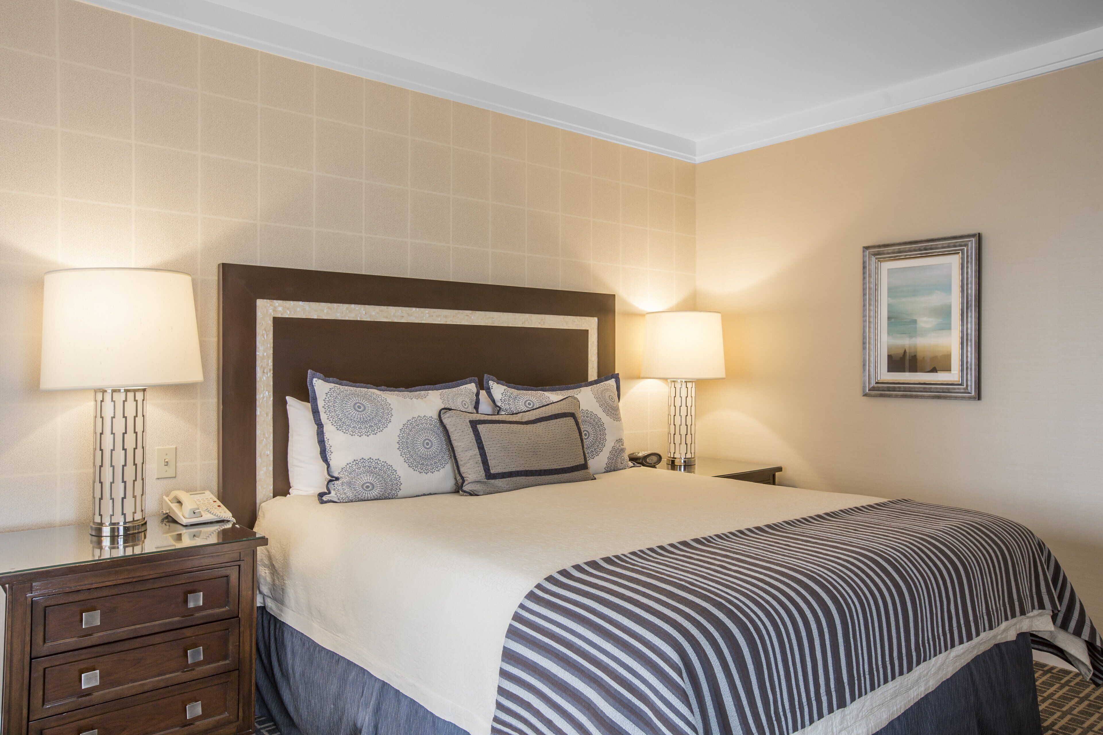 A neatly made bed with patterned pillows, a striped blanket, and bedside lamps.