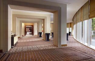 A hotel corridor with patterned carpet, large windows, and a central area with a door and lights.