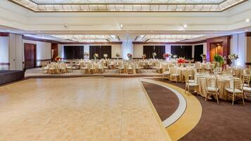 A large ballroom with a polished wooden floor, round tables with chairs, and floral centerpieces.