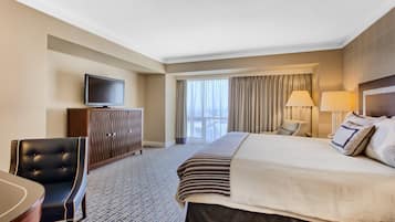 Quarto de hotel com uma cama grande, televisão, escrivaninha e cadeira.