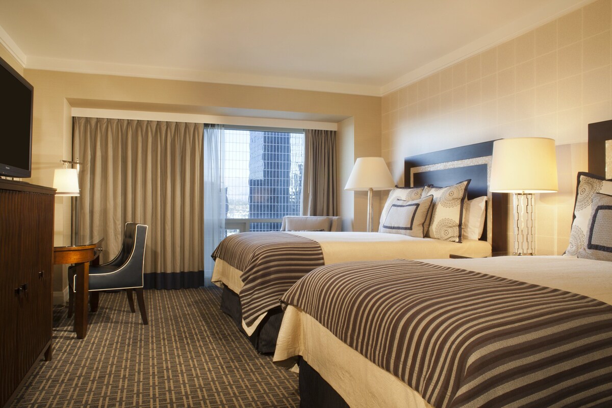 A hotel room with two beds, a TV, a desk, and a chair.
