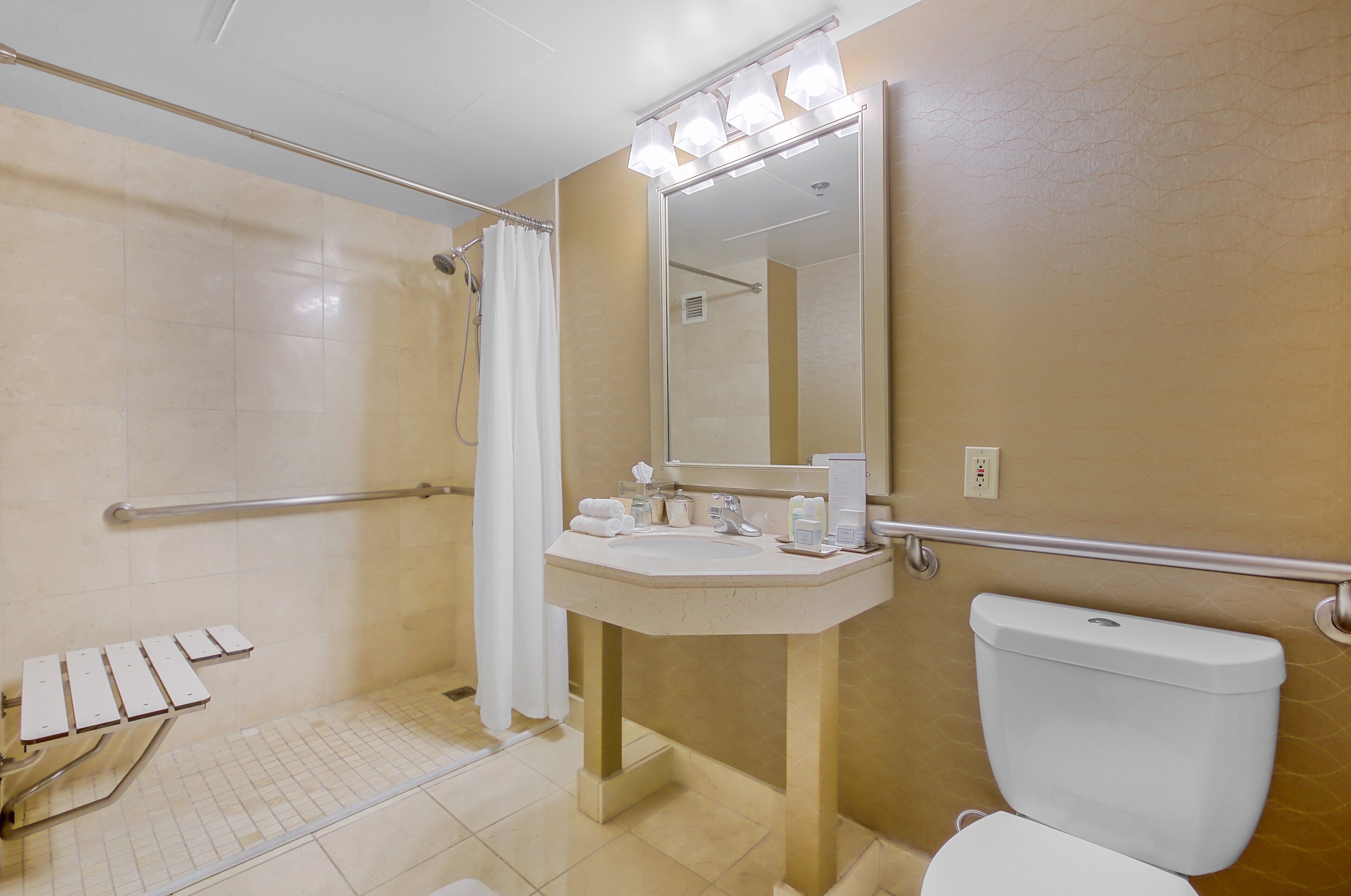 A bathroom with a shower, a sink, a toilet, and a mirror with lights.