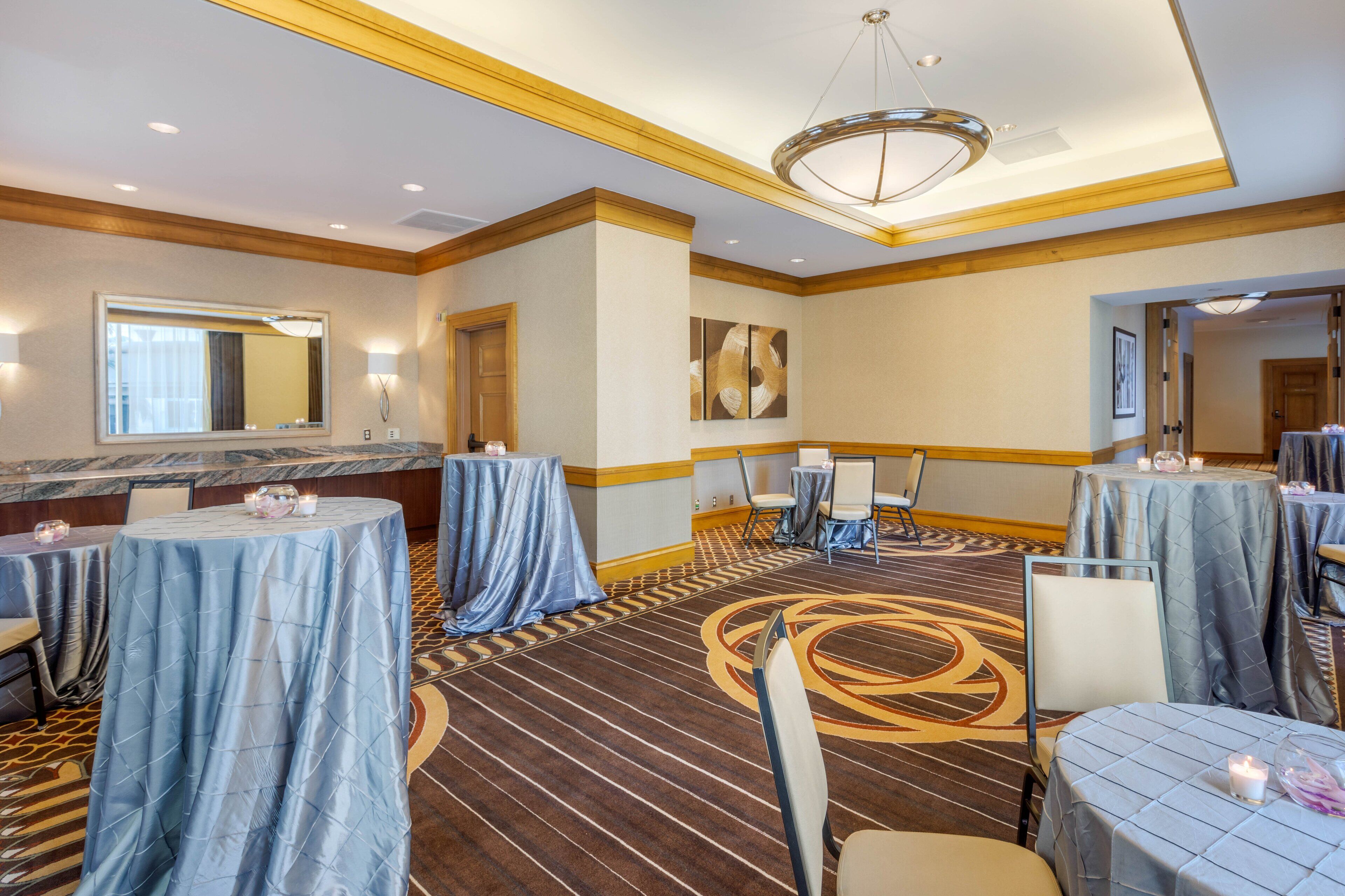 A hotel conference room with round tables, chairs, and a carpeted floor.