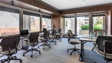 Una sala de conferencias moderna con ventanas amplias, piso alfombrado y una mesa con sillas y un ordenador portátil.