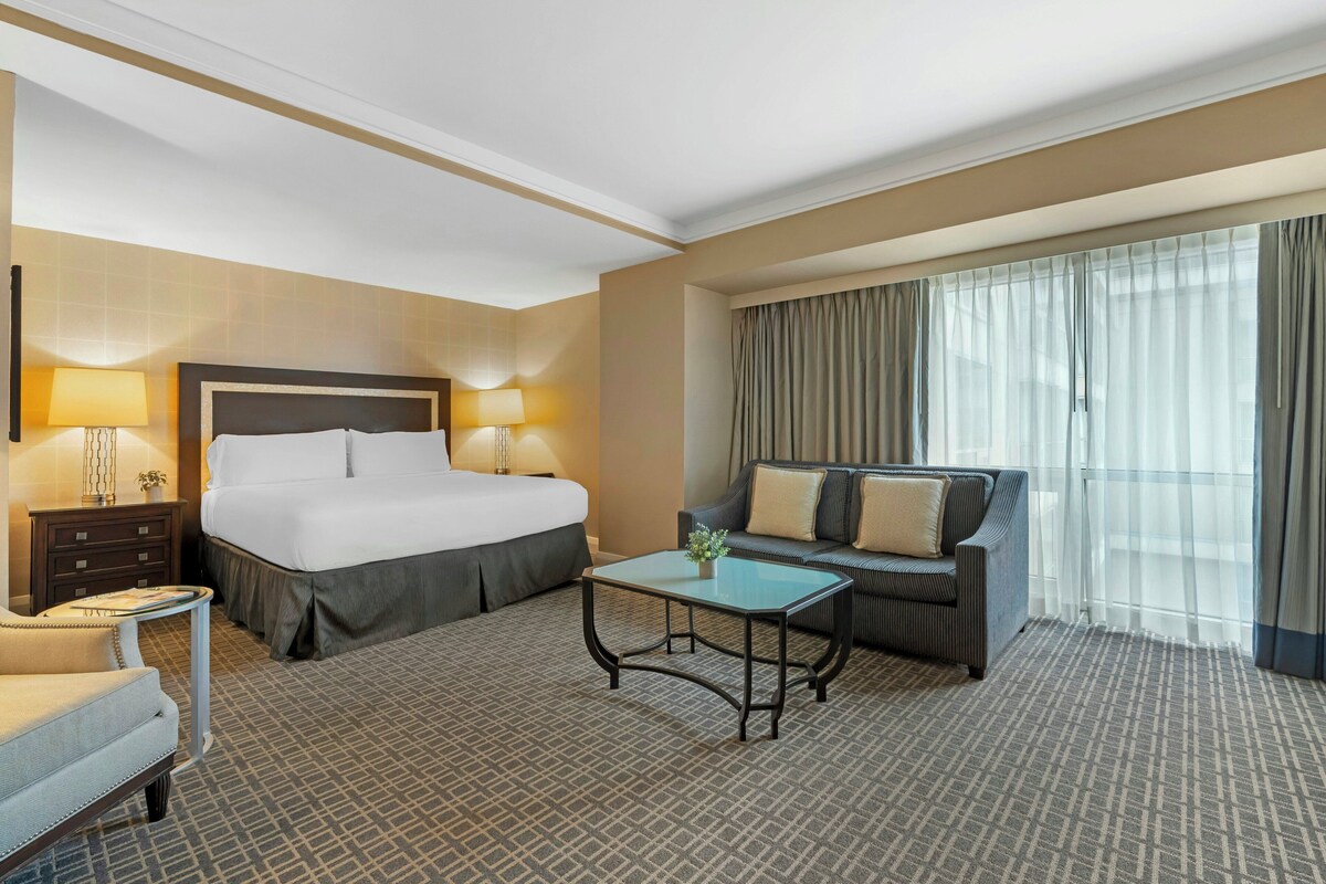 A hotel room with a large bed, a sofa, a small table, and a nightstand.