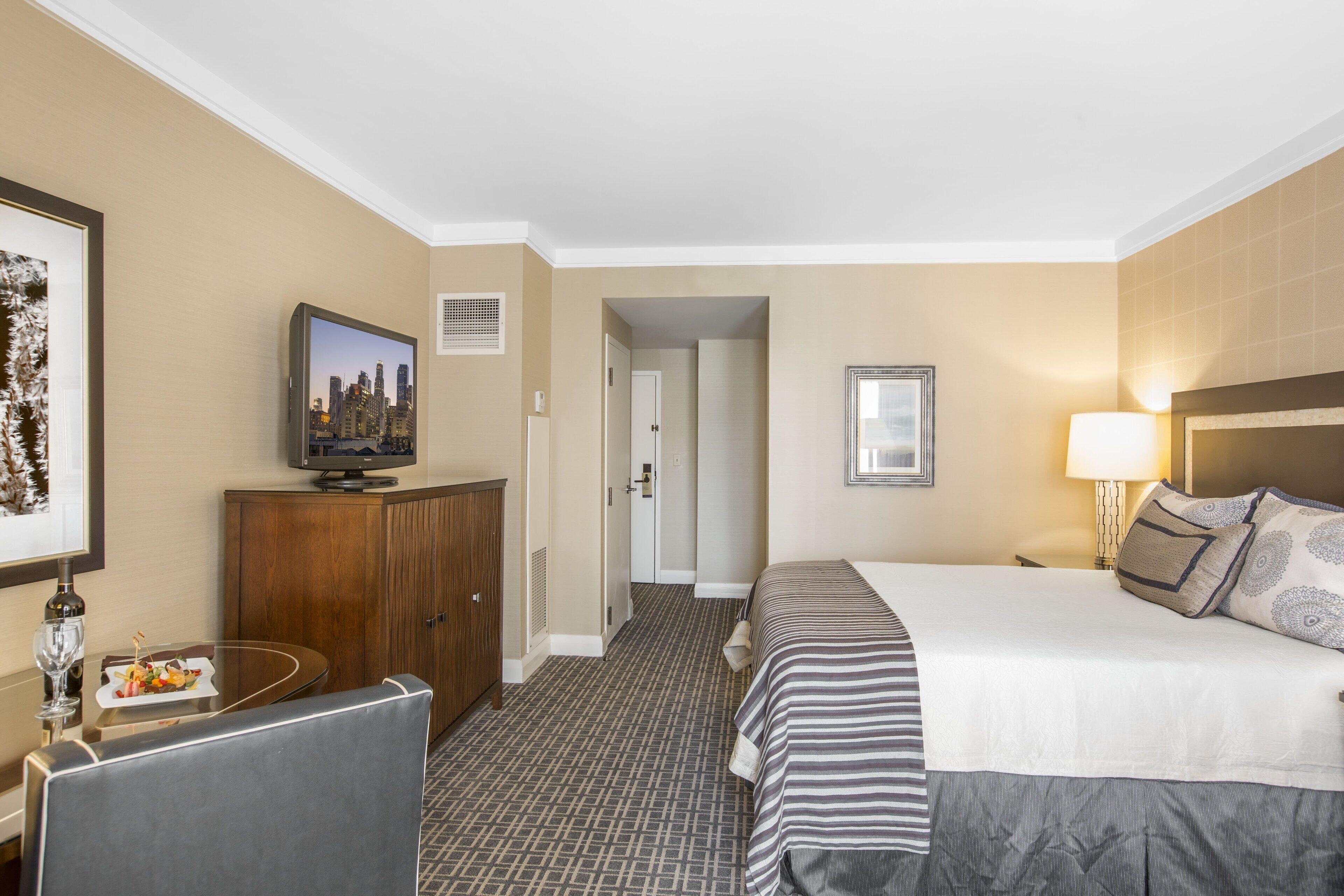 A hotel room with a bed, a television, a desk with a chair, and a dining table with a plate of food.