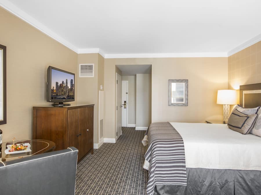 Quarto de hotel com cama, televisão, escrivaninha e cadeira, e uma mesa de jantar com um prato de comida.
