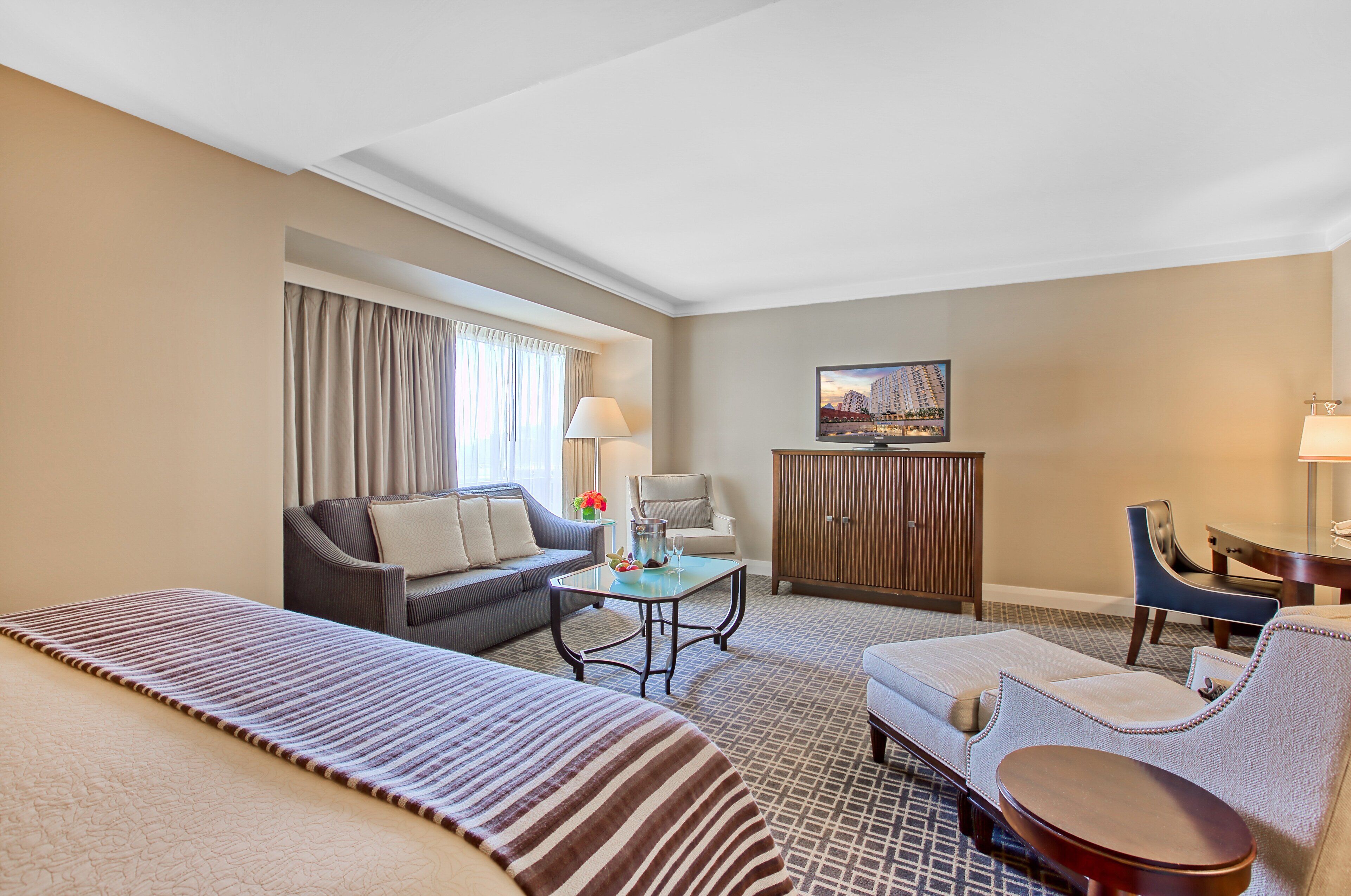 Una habitación de hotel con cama, sofá, sillón, mesita, armario y televisor.