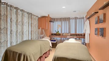 Two single beds with green bedspreads, a bedside table, and a large window with sheer curtains.