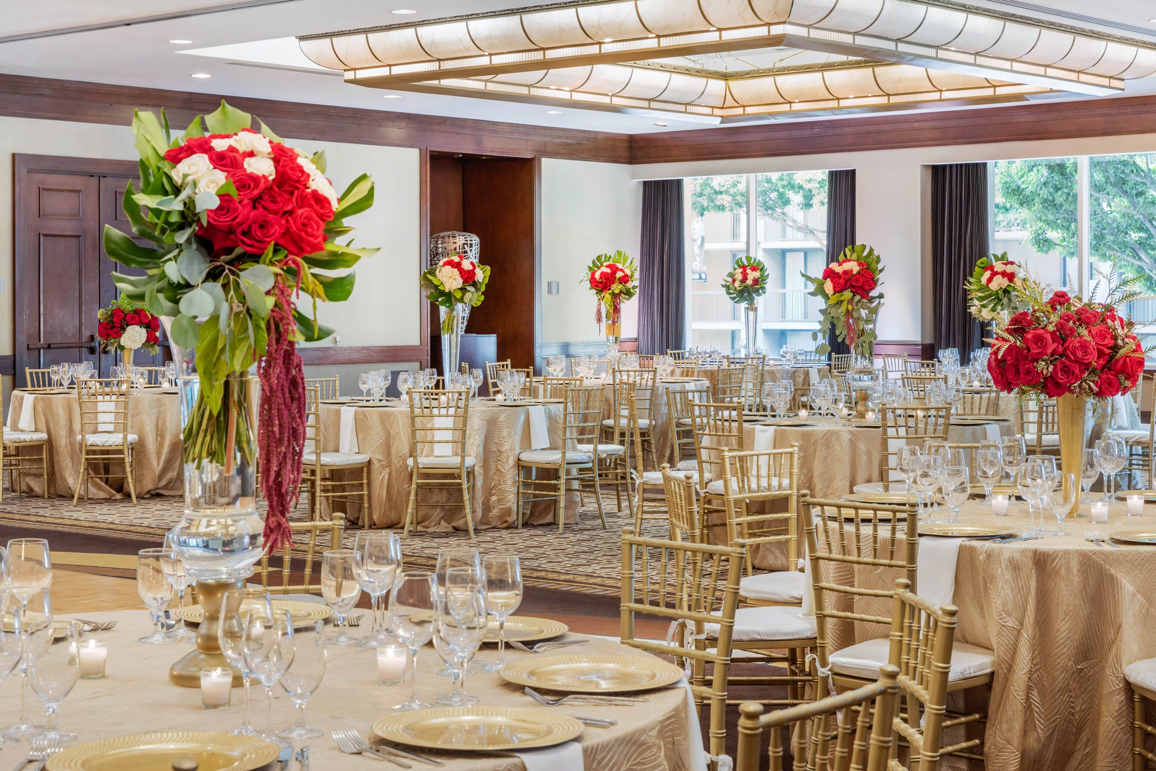Een feestzaal met ronde tafels voor een diner, elk met gouden tafelkleden en witte stoelen.
