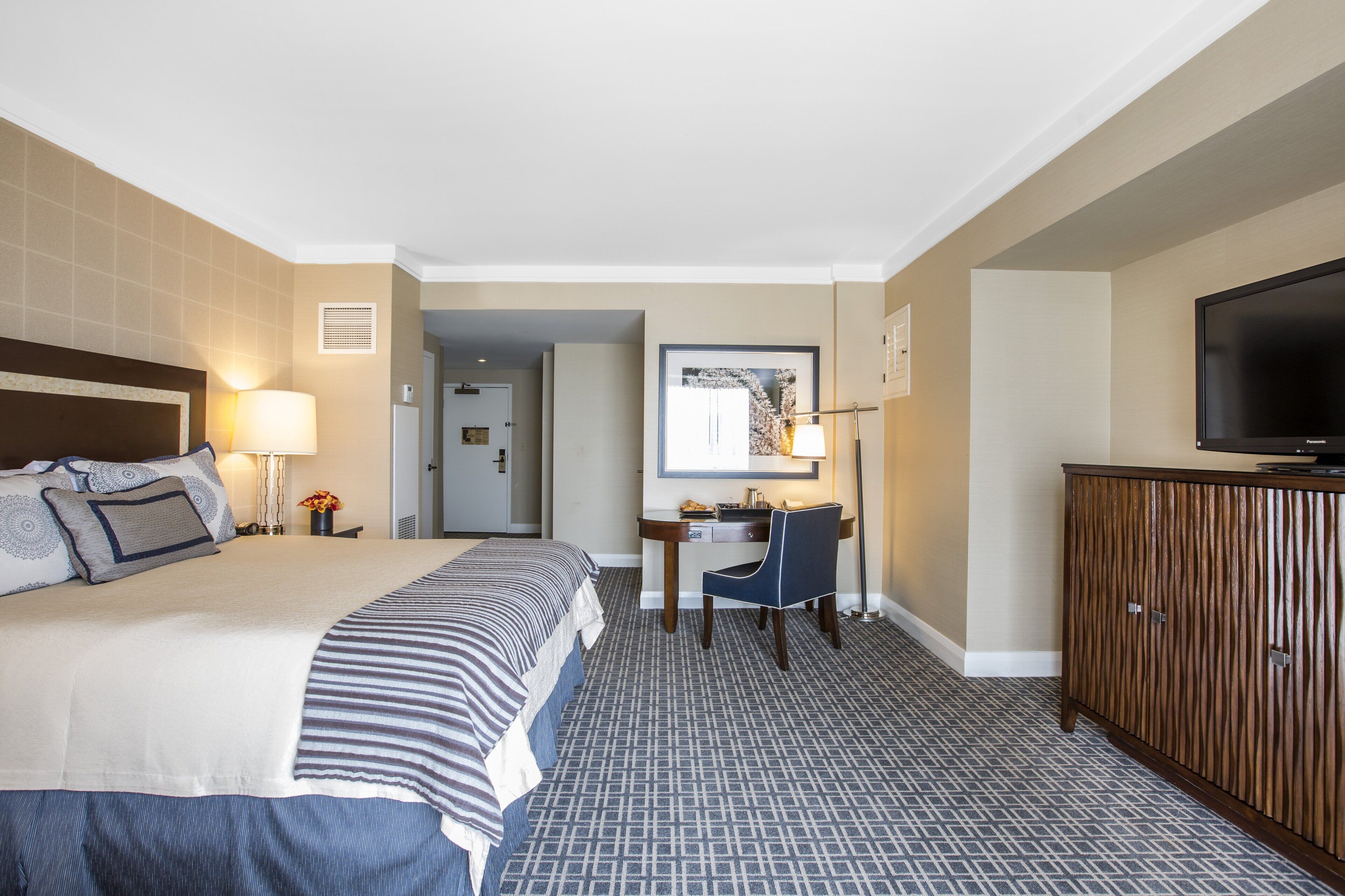 Quarto de hotel com uma cama grande, uma escrivaninha, uma cadeira, uma televisão e um guarda-roupa.