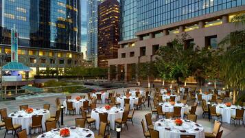 A rooftop dining area with tables set for guests, surrounded by modern buildings and a landscaped garden.