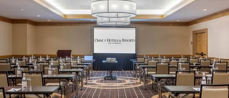 A conference room with a large screen displaying "OMNI HOTELS & RESORTS los angeles", rows of tables with chairs, and a patterned carpet.