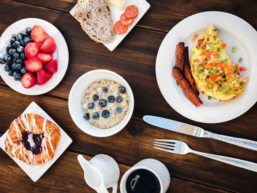 Une table dressée pour le petit-déjeuner, avec différents plats, notamment des toasts, des œufs, du bacon, des fraises, des myrtilles et un croissant.