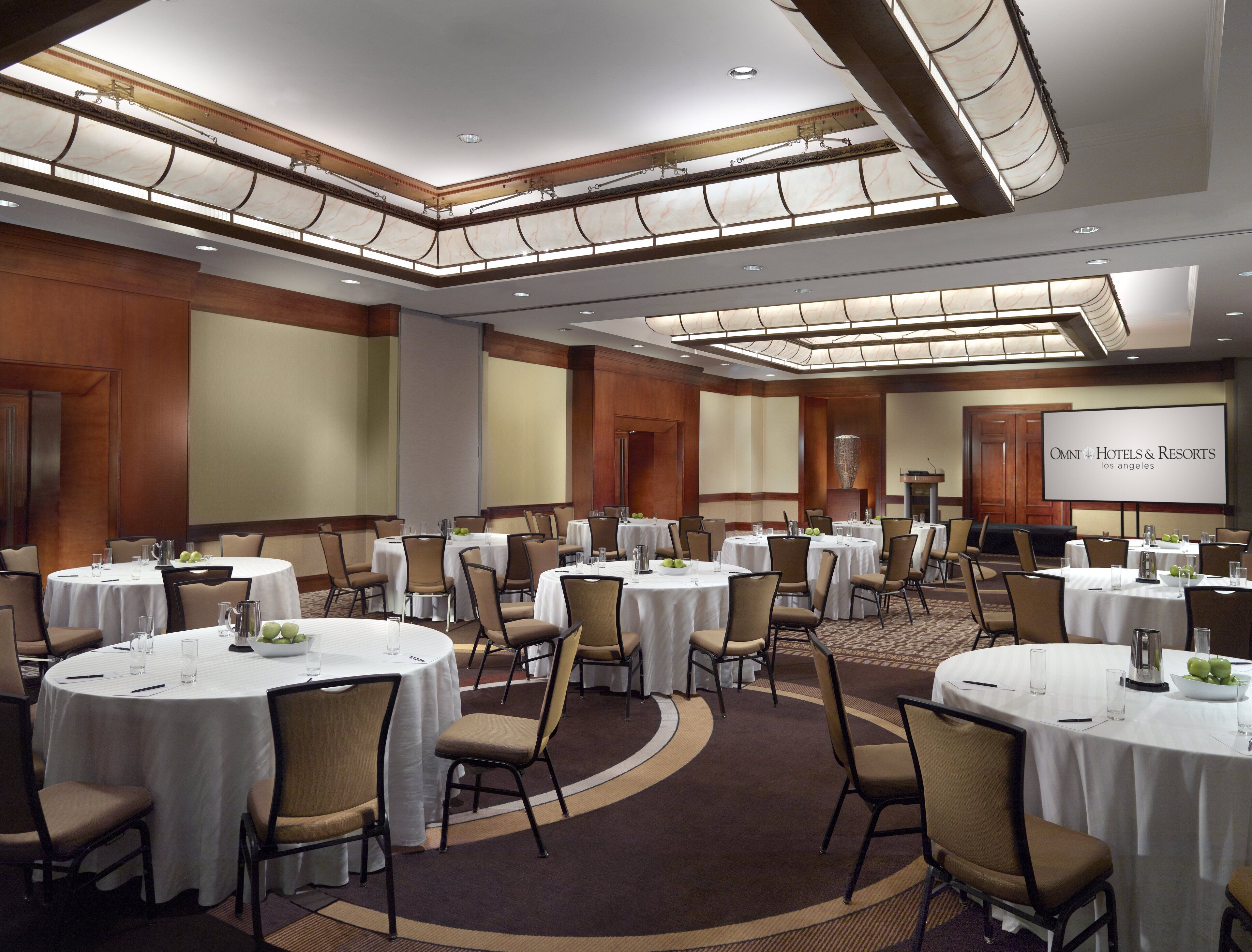Une salle de conférence équipée de plusieurs tables rondes, de chaises et d’un grand écran affichant le texte « OMNI Hotels & Resorts Los Angeles ».