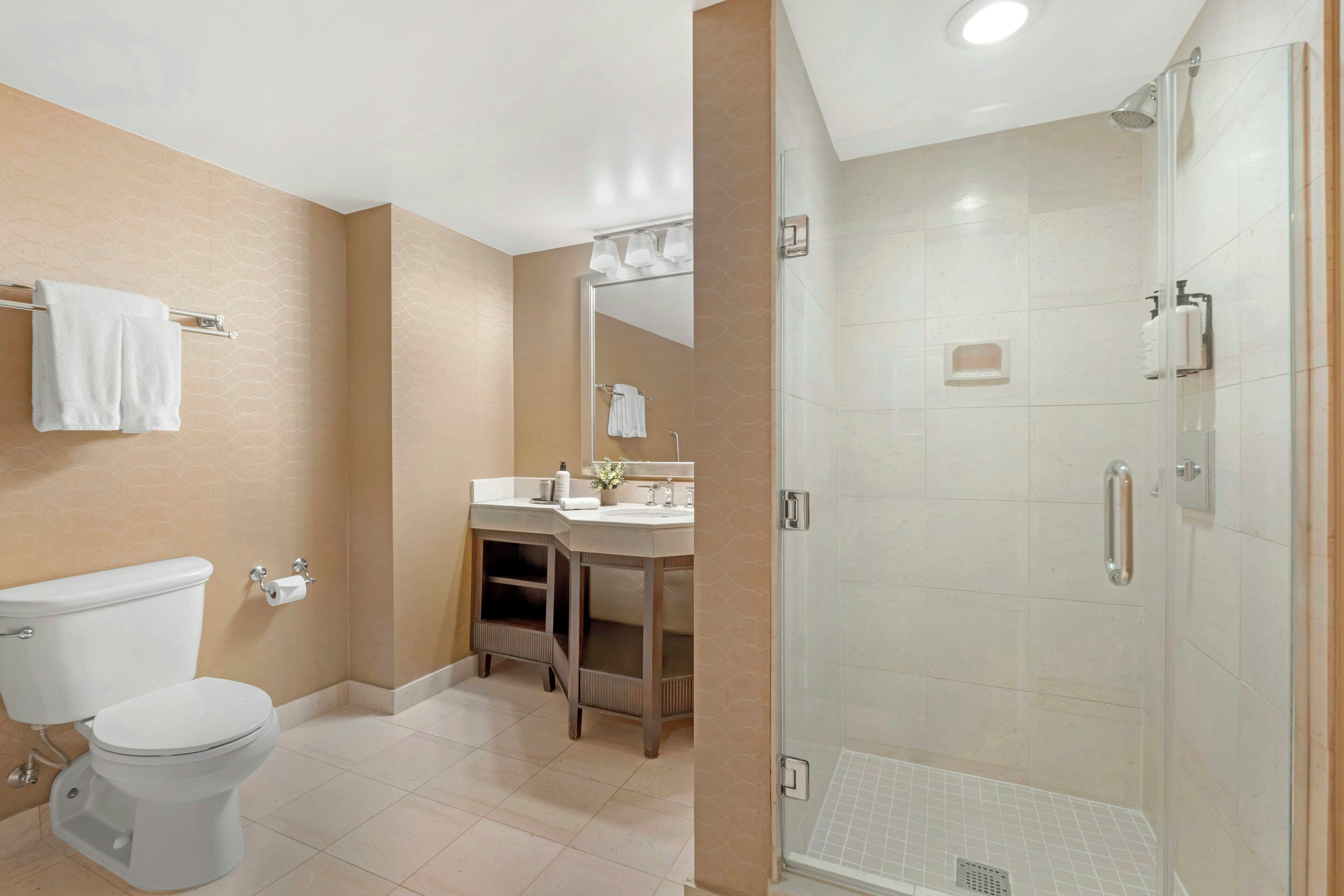 A modern bathroom with a toilet, sink, mirror, and shower.