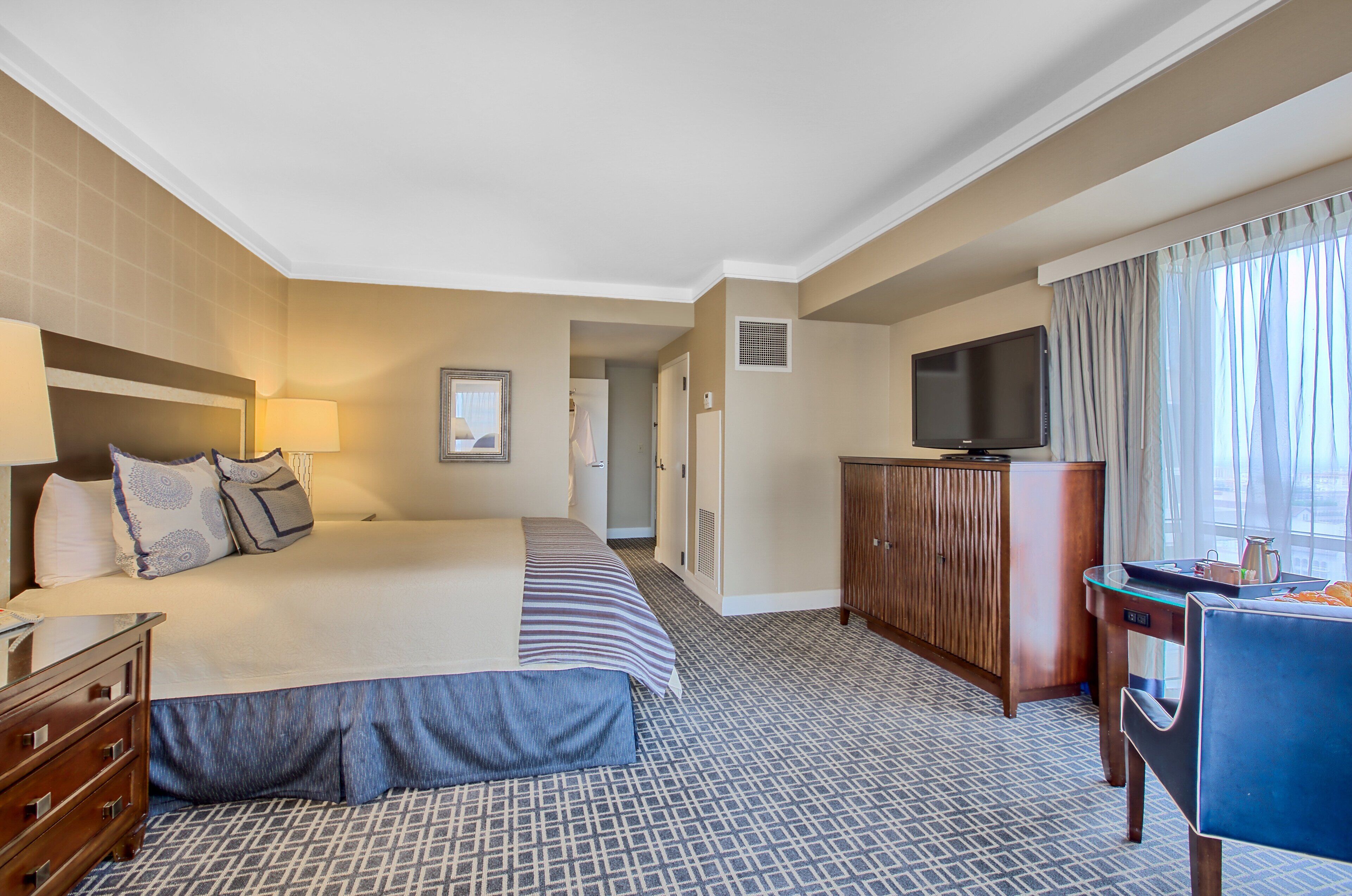 Une chambre d’hôtel avec un grand lit, un bureau avec une chaise, une télévision et une armoire.