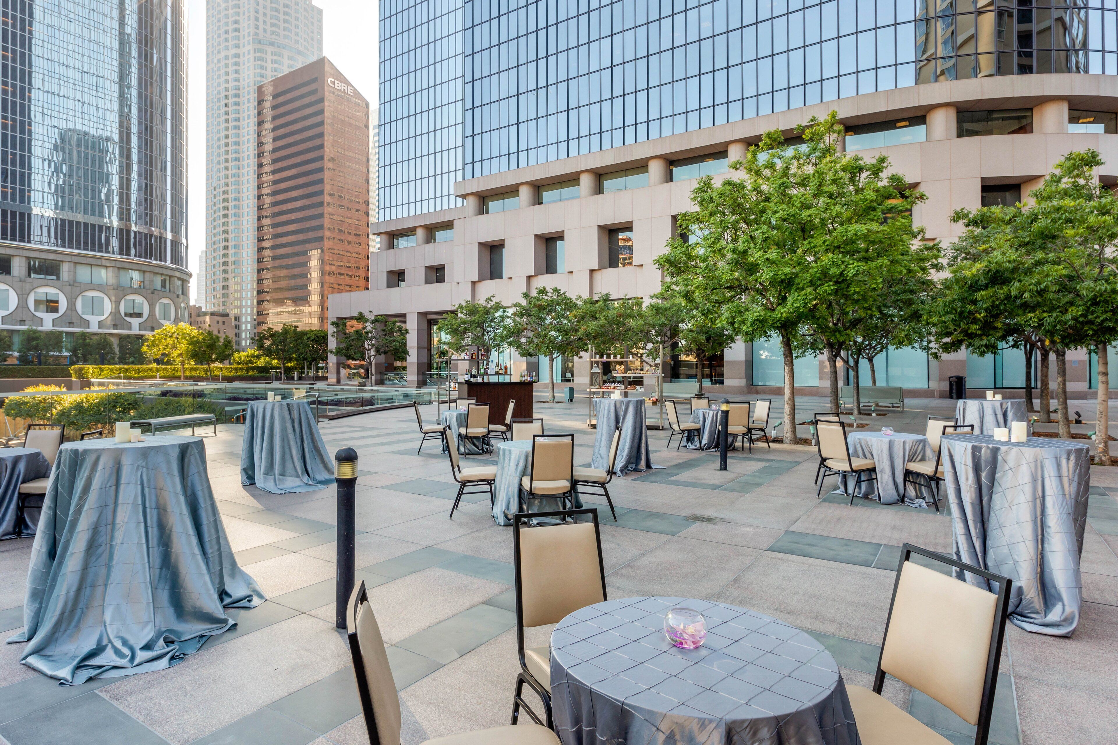 An outdoor dining area with tables and chairs, surrounded by trees and buildings.