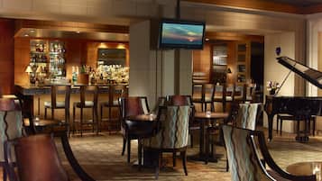 A bar area with a television, bar stools, and a piano.