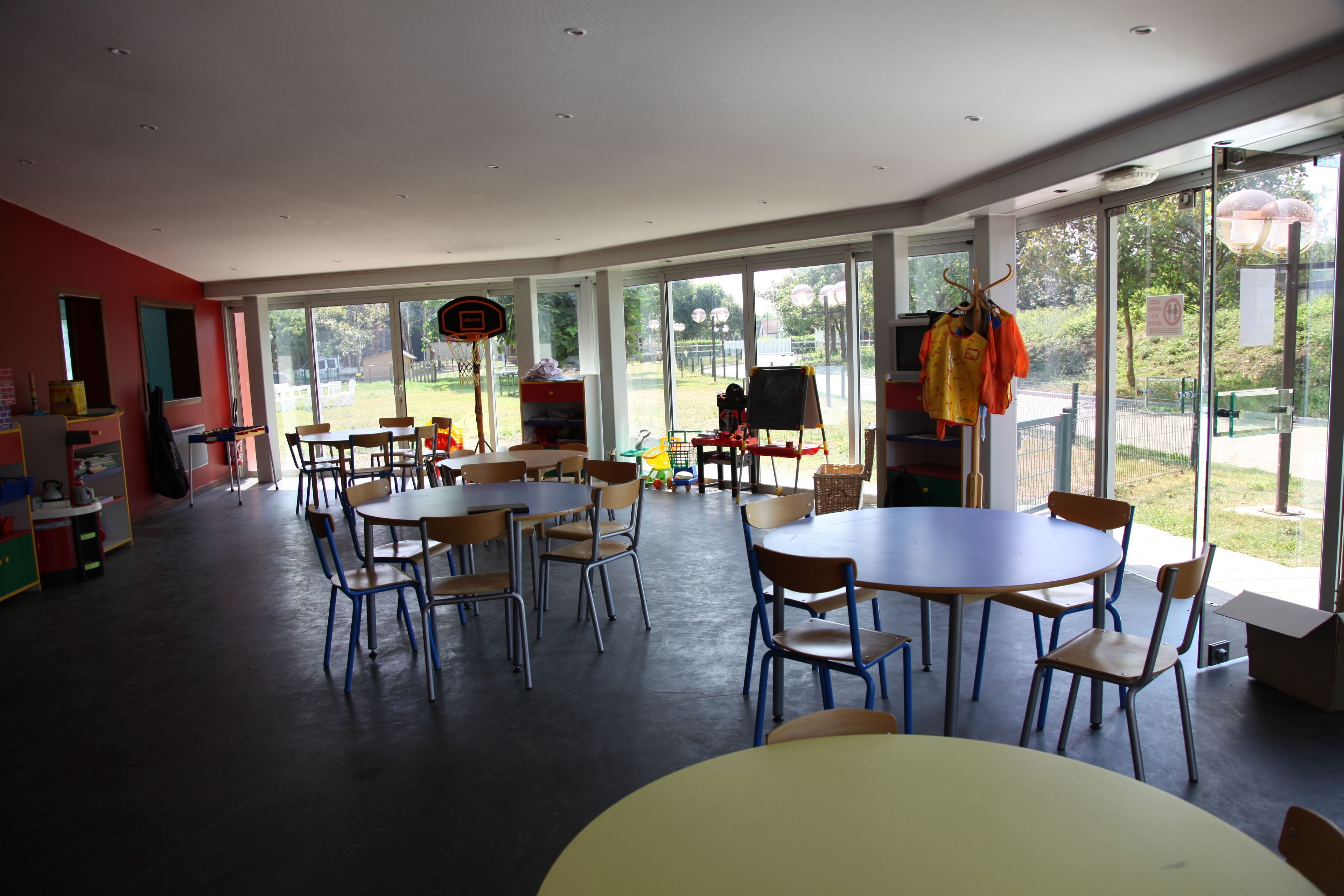 Un grand espace intérieur aménagé avec des tables et des chaises, de grandes fenêtres et un panier de basketball.