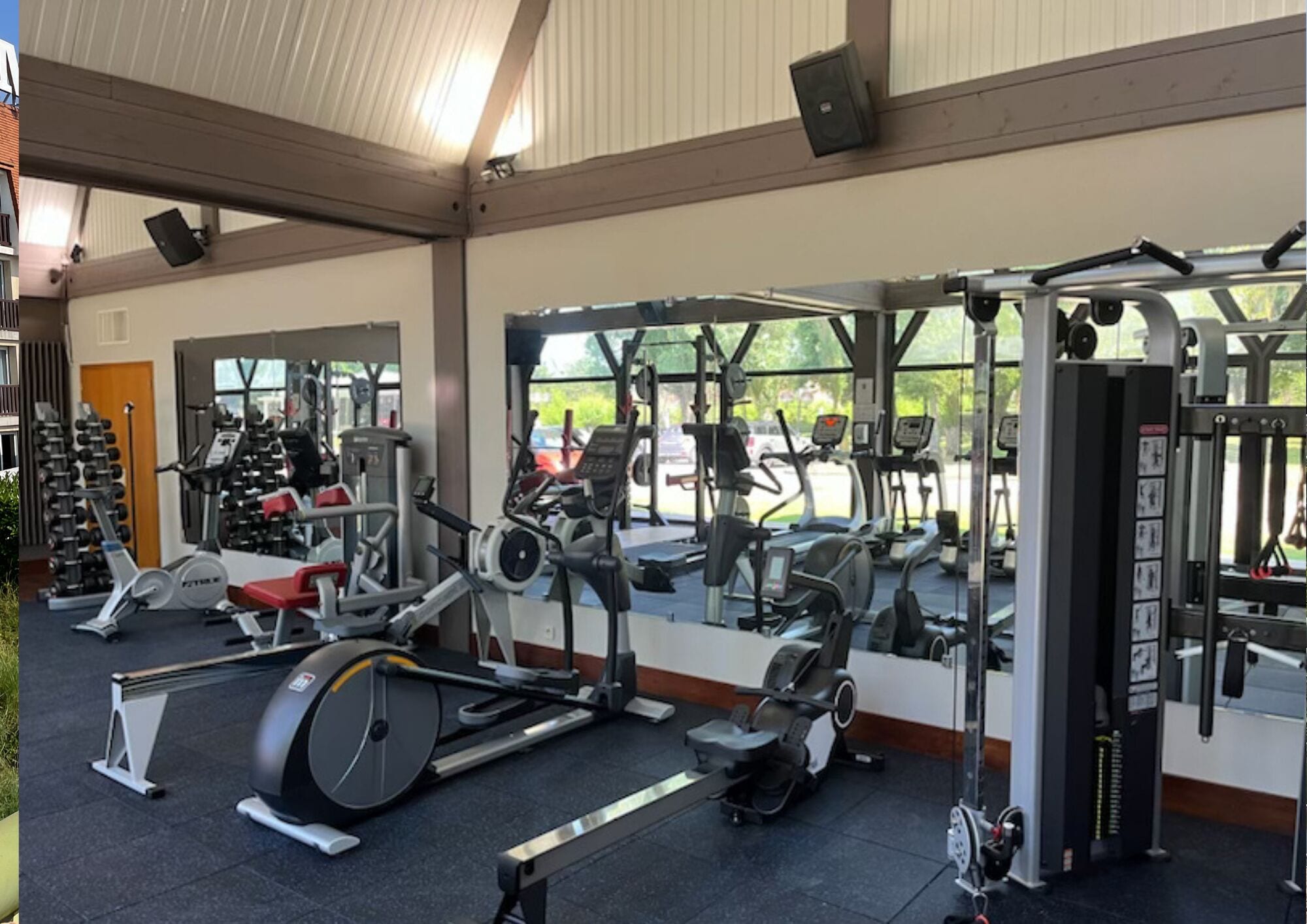 A gym with various exercise equipment, large windows, and a mirrored wall.