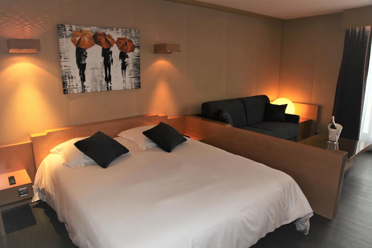 A hotel room with a large bed, two bedside tables, a nightstand, a wall-mounted artwork, and a separate seating area with a sofa and a lamp.