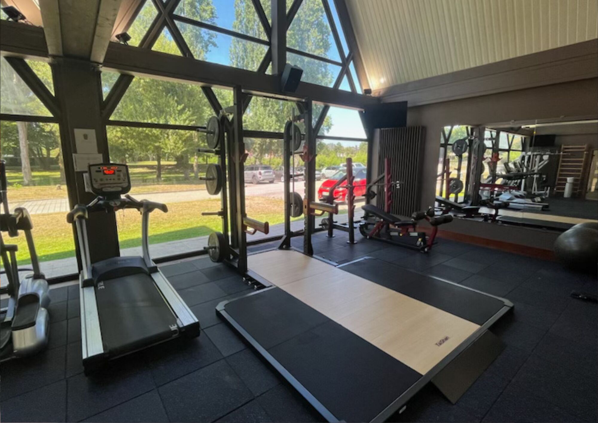 Un gimnasio con equipo cardiovascular, máquinas de pesas y amplios ventanales con vistas al exterior.