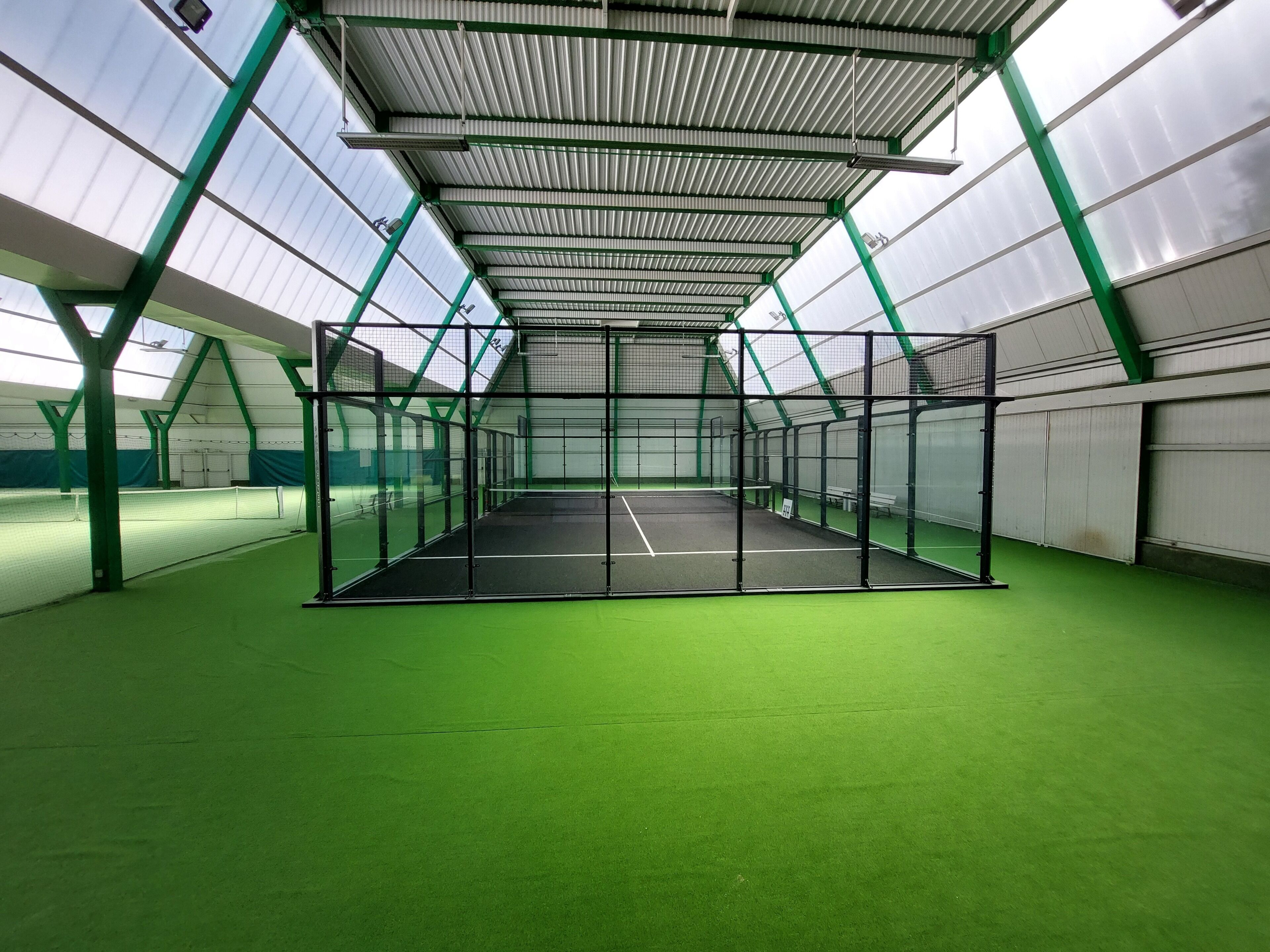 Una cancha de tenis cubierta con superficie verde, rodeada por una estructura de metal y vidrio.