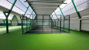 Una cancha de tenis cubierta con superficie verde, rodeada por una estructura de metal y vidrio.