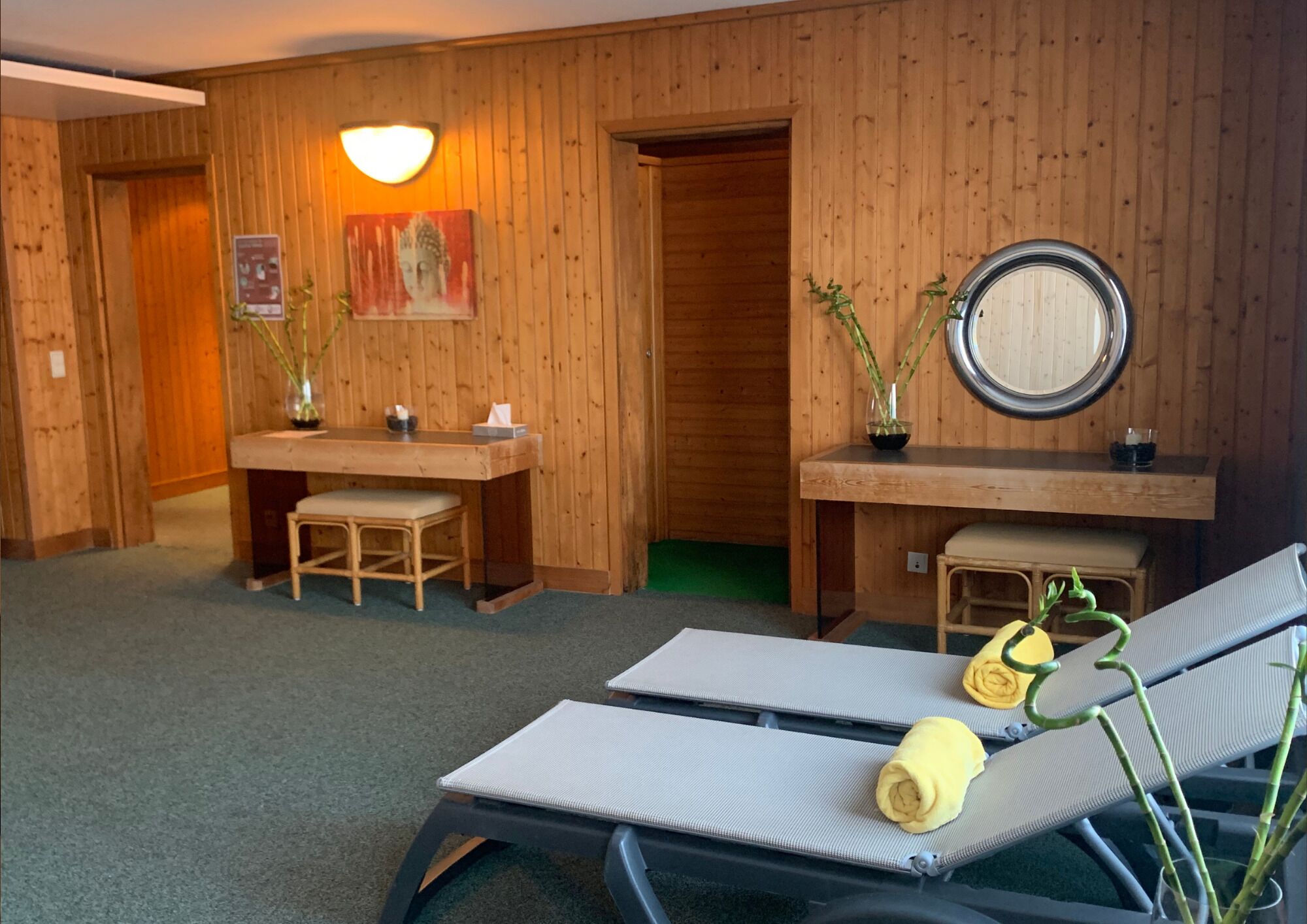 Ein Zimmer mit Holzwänden, einem Schreibtisch mit Stuhl, einem kleinen Tisch mit Vase sowie zwei Liegestühlen mit Handtüchern.