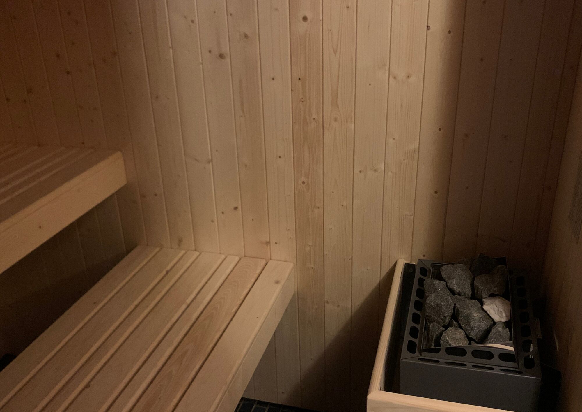 A wooden sauna with benches and a stone-filled container.